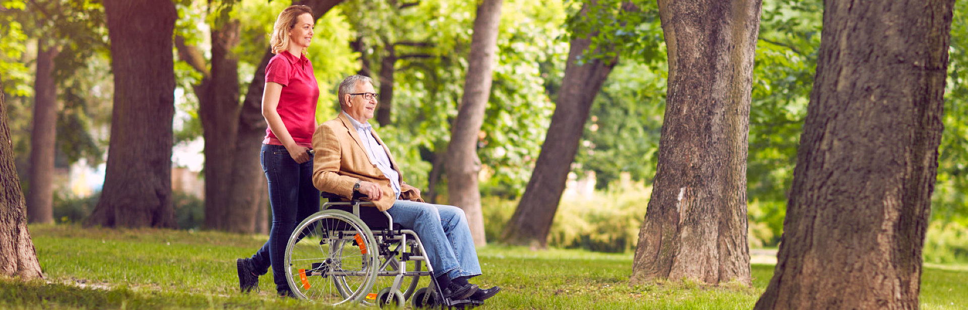 elderly man sitting on a wheelchair assist by a caregiver